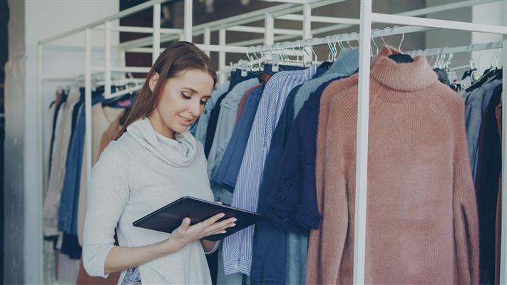 Shop owner checking product information on a tablet beside clothing racks